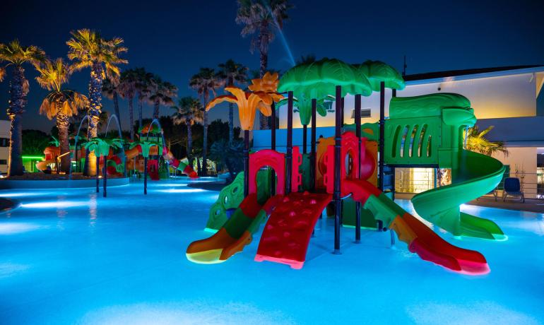 Night water park with colorful slides and lit palm trees.