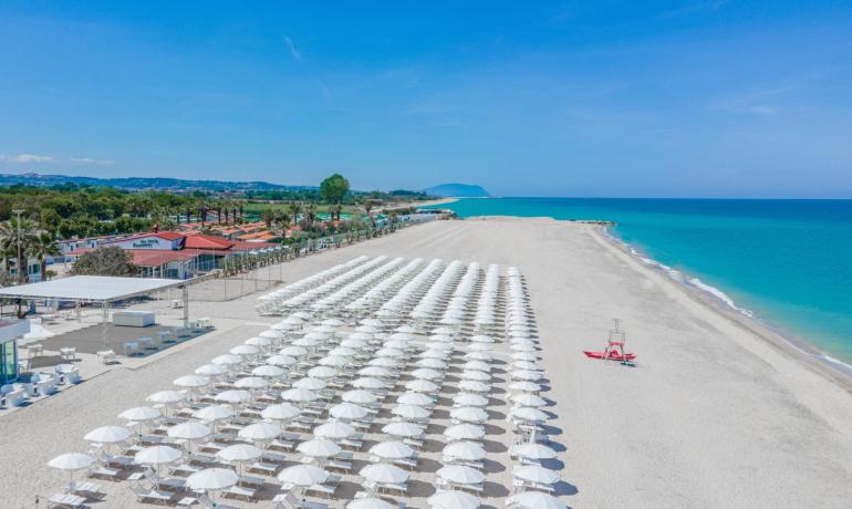 Strand mit weißen Sonnenschirmen und blauem Meer, sonniger Tag.