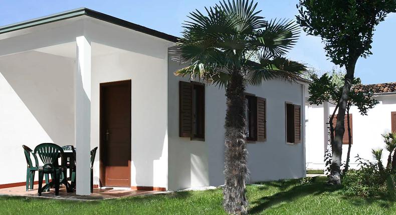 Bungalow bianco con palme e sedie verdi all'esterno.