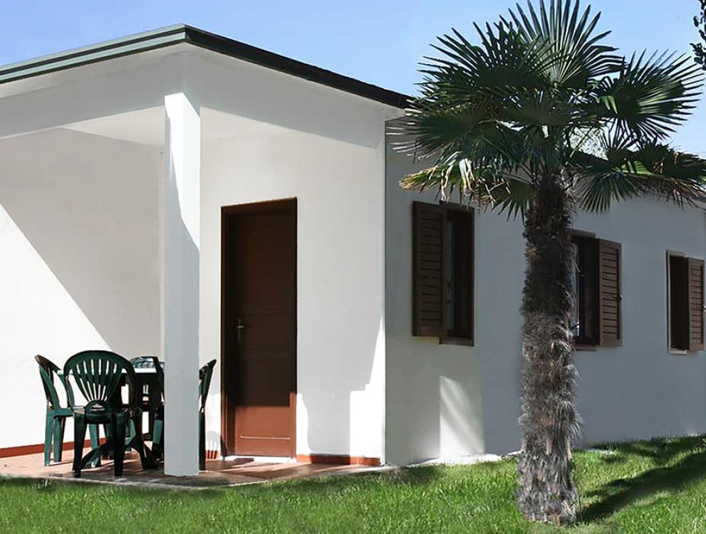 Bungalow bianco con palme e sedie verdi all'esterno.